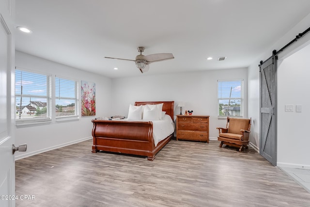 bedroom with a barn door, light hardwood / wood-style floors, and ceiling fan