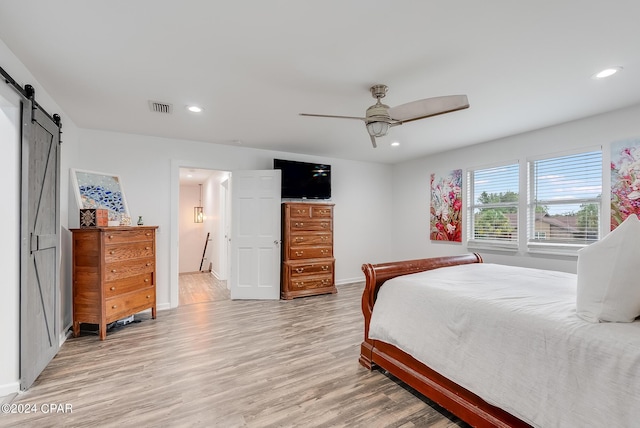 bedroom with a barn door, ceiling fan, and light wood-type flooring