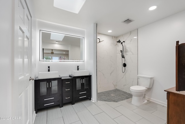 bathroom with a skylight, a tile shower, vanity, ceiling fan, and toilet