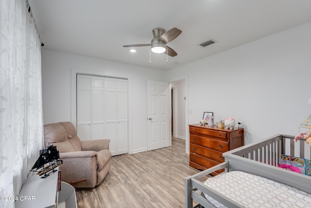 bedroom with ceiling fan, a closet, light hardwood / wood-style floors, and a nursery area