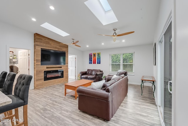 living room featuring ceiling fan, a large fireplace, light wood-type flooring, and vaulted ceiling