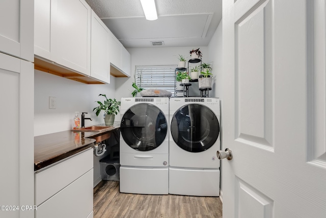 clothes washing area with cabinets, sink, independent washer and dryer, light wood-type flooring, and a textured ceiling