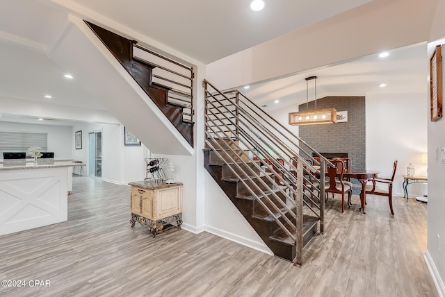 staircase with hardwood / wood-style flooring, lofted ceiling, and a brick fireplace