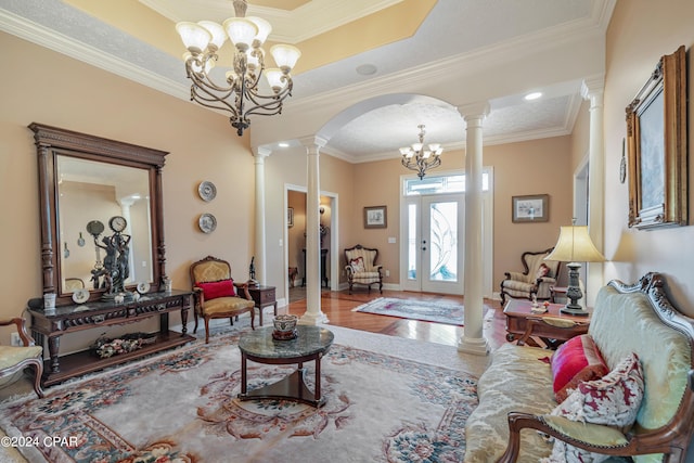 living room with wood finished floors, arched walkways, an inviting chandelier, crown molding, and ornate columns