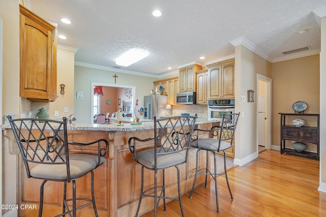 kitchen featuring a breakfast bar area, visible vents, stainless steel appliances, tasteful backsplash, and light wood-type flooring