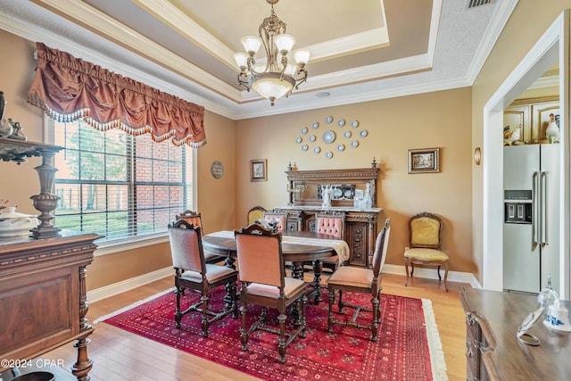 dining space with baseboards, light wood finished floors, a tray ceiling, ornamental molding, and a chandelier