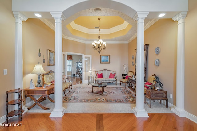 living area featuring baseboards, wood-type flooring, crown molding, decorative columns, and a raised ceiling