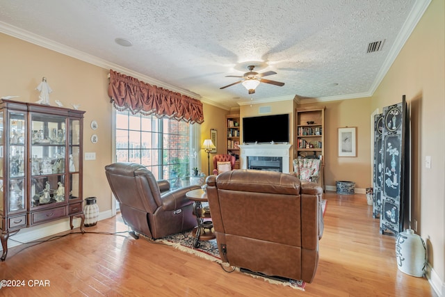 living room with light wood-type flooring, a ceiling fan, a fireplace, and crown molding