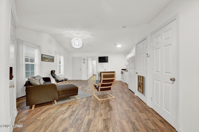 living room featuring an inviting chandelier, wood-type flooring, and vaulted ceiling