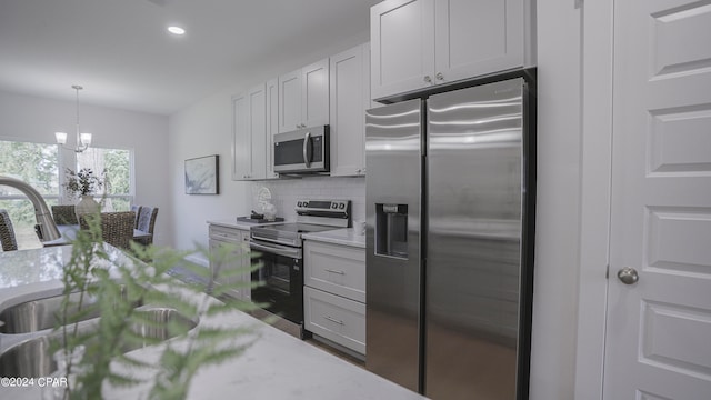 kitchen featuring pendant lighting, white cabinetry, stainless steel appliances, light stone countertops, and decorative backsplash