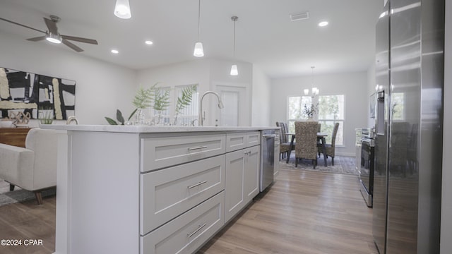 kitchen with light hardwood / wood-style floors, hanging light fixtures, stainless steel appliances, a center island with sink, and ceiling fan