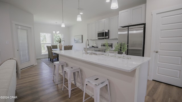 kitchen with a kitchen island with sink, tasteful backsplash, white cabinetry, hanging light fixtures, and stainless steel appliances