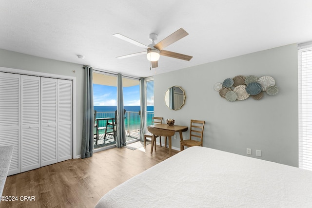 bedroom featuring a closet, access to outside, a water view, hardwood / wood-style floors, and ceiling fan