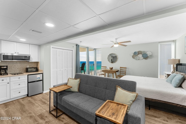 bedroom featuring ceiling fan, a closet, a drop ceiling, light hardwood / wood-style floors, and a water view