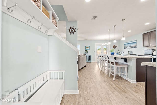 kitchen with hanging light fixtures, a kitchen bar, an inviting chandelier, dark brown cabinets, and light hardwood / wood-style flooring