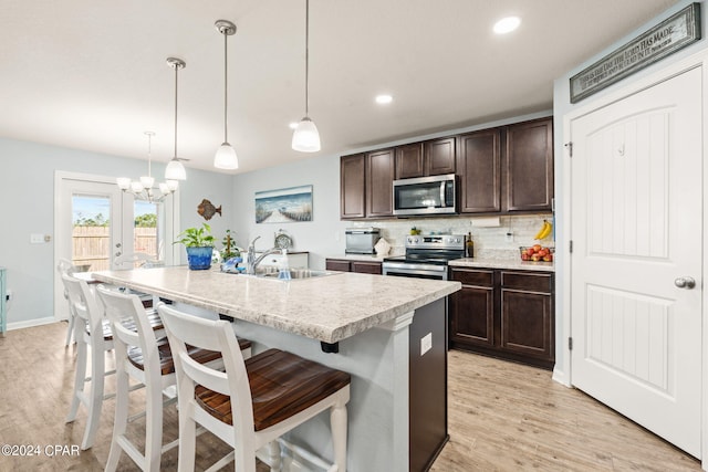 kitchen featuring hanging light fixtures, sink, a center island with sink, stainless steel appliances, and light hardwood / wood-style floors