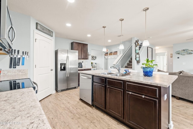 kitchen featuring appliances with stainless steel finishes, hanging light fixtures, an island with sink, light hardwood / wood-style flooring, and sink