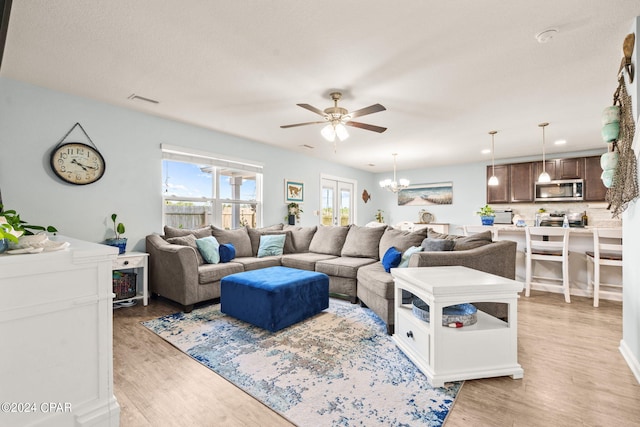 living room with ceiling fan with notable chandelier and light hardwood / wood-style flooring