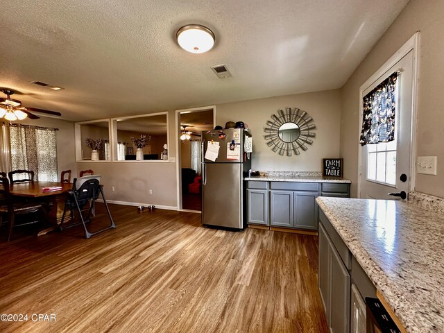 kitchen featuring ceiling fan, stainless steel fridge, gray cabinetry, a textured ceiling, and light wood-type flooring