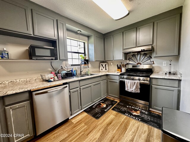 kitchen with a textured ceiling, sink, hanging light fixtures, light hardwood / wood-style flooring, and stainless steel appliances