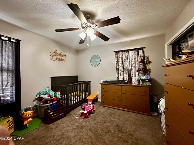 carpeted bedroom with a crib, a textured ceiling, and ceiling fan