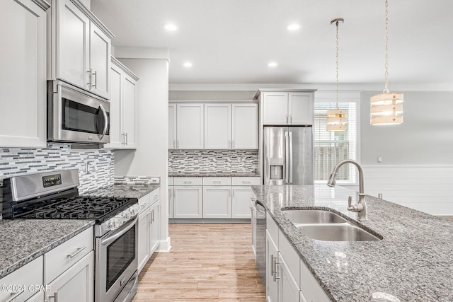 kitchen with sink, stainless steel appliances, white cabinets, stone countertops, and decorative light fixtures