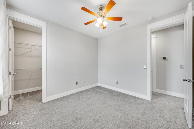 unfurnished bedroom with ceiling fan, a walk in closet, a closet, and light carpet