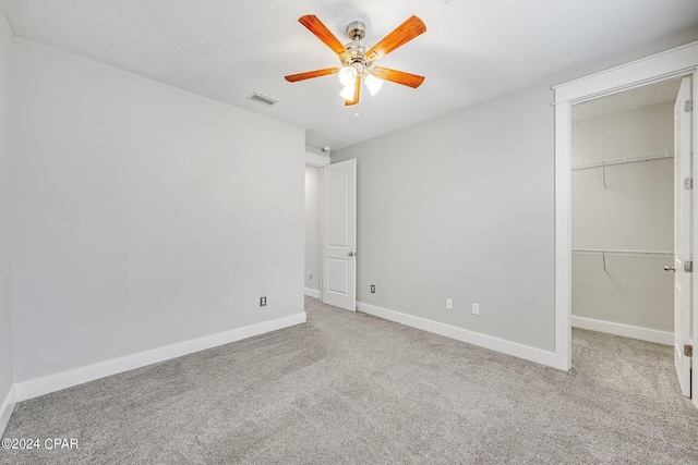 unfurnished bedroom featuring ceiling fan, light colored carpet, a closet, and a walk in closet