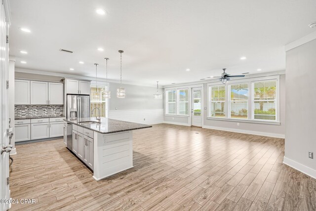 kitchen with decorative light fixtures, an island with sink, dark stone countertops, stainless steel appliances, and light hardwood / wood-style flooring