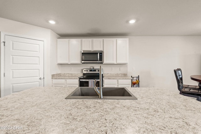 kitchen featuring light stone counters, white cabinets, appliances with stainless steel finishes, and sink