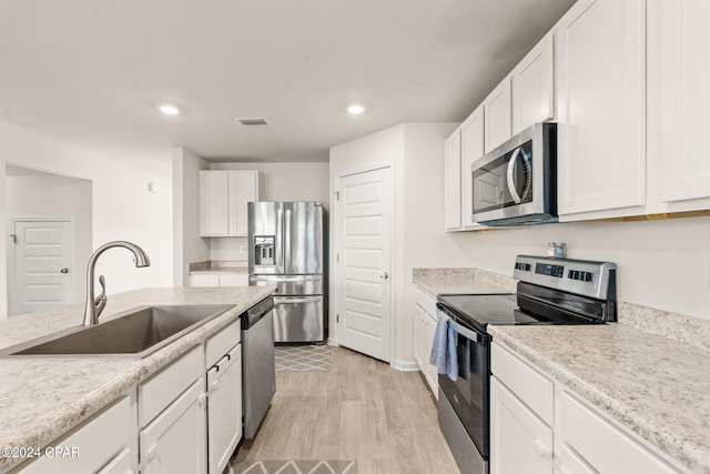 kitchen featuring light stone counters, white cabinets, sink, light hardwood / wood-style flooring, and appliances with stainless steel finishes