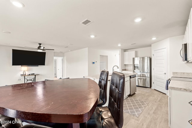 dining area with light wood-type flooring, sink, and ceiling fan