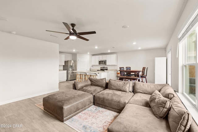 living room with light wood-type flooring, ceiling fan, and sink