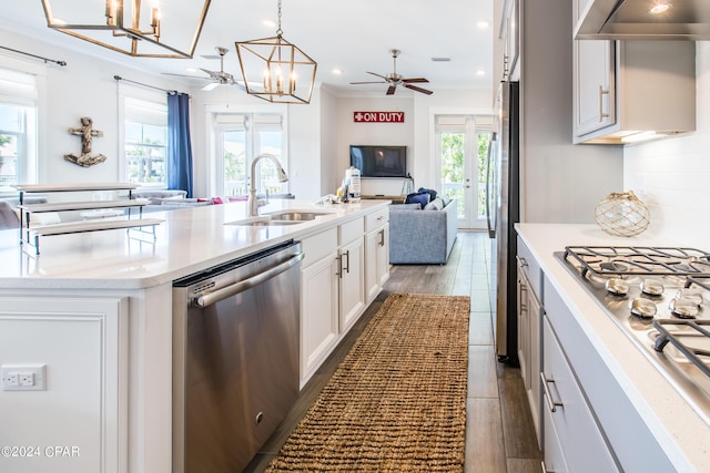 kitchen with decorative light fixtures, white cabinetry, stainless steel appliances, sink, and a center island with sink