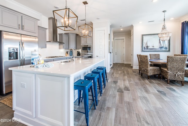 kitchen with light countertops, gray cabinetry, appliances with stainless steel finishes, a sink, and wall chimney exhaust hood