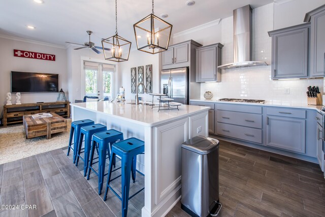 kitchen with sink, wall chimney range hood, stainless steel appliances, and an island with sink