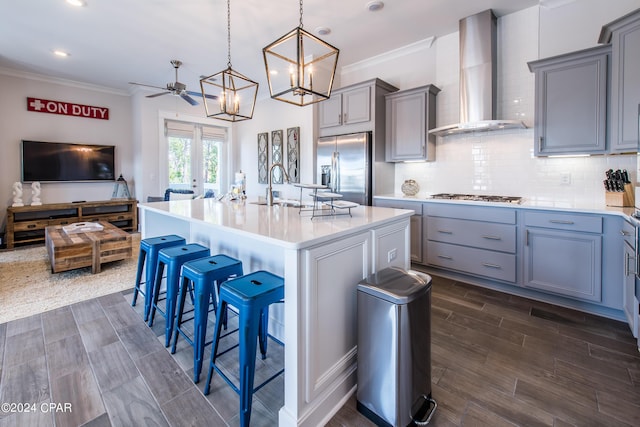 kitchen with a breakfast bar, stainless steel appliances, gray cabinetry, a sink, and wall chimney exhaust hood