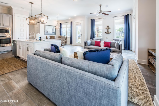 living room featuring sink, a wealth of natural light, ceiling fan with notable chandelier, and ornamental molding