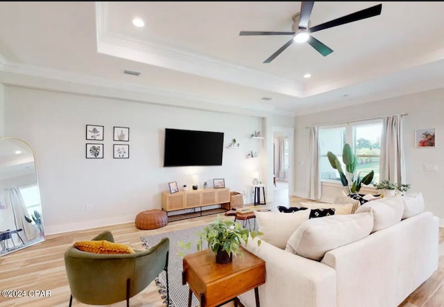 living room with ceiling fan, light hardwood / wood-style flooring, crown molding, and a tray ceiling