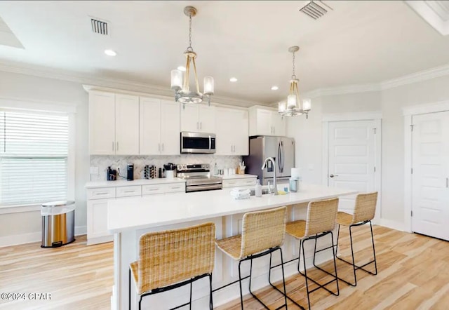 kitchen featuring an inviting chandelier, appliances with stainless steel finishes, a kitchen island with sink, and white cabinetry