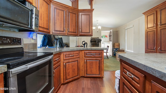 kitchen featuring ornamental molding, hardwood / wood-style flooring, stainless steel appliances, washing machine and dryer, and a notable chandelier