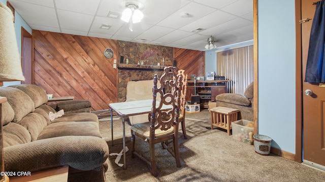 carpeted living room with ceiling fan, a drop ceiling, and wood walls