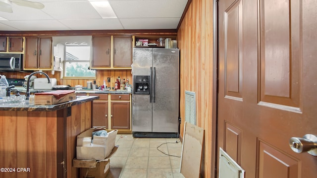 kitchen featuring appliances with stainless steel finishes, light tile patterned floors, ceiling fan, a paneled ceiling, and wooden walls