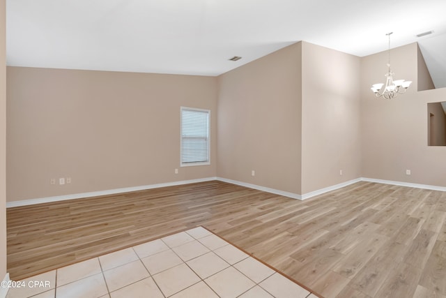 spare room featuring vaulted ceiling, light hardwood / wood-style flooring, and a chandelier