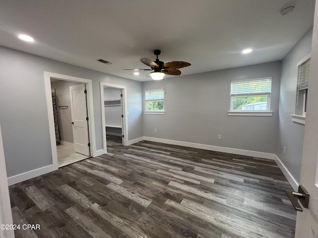 unfurnished bedroom featuring dark hardwood / wood-style floors, a closet, a walk in closet, and multiple windows