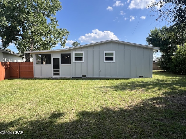 rear view of house featuring board and batten siding, fence, and a lawn
