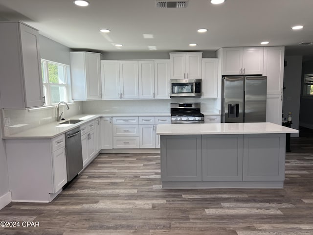 kitchen with hardwood / wood-style flooring, sink, white cabinetry, a kitchen island, and stainless steel appliances