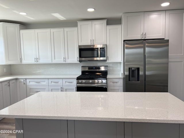 kitchen featuring white cabinets, stainless steel appliances, tasteful backsplash, and light stone countertops