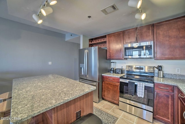 kitchen with light stone counters, light tile patterned flooring, appliances with stainless steel finishes, and a center island