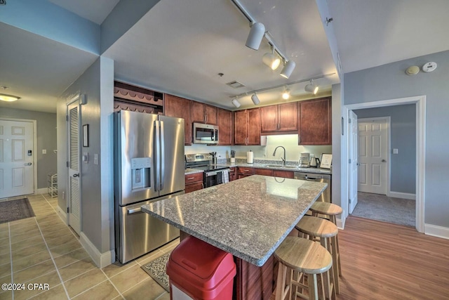 kitchen with a breakfast bar, stainless steel appliances, a center island, light hardwood / wood-style flooring, and sink